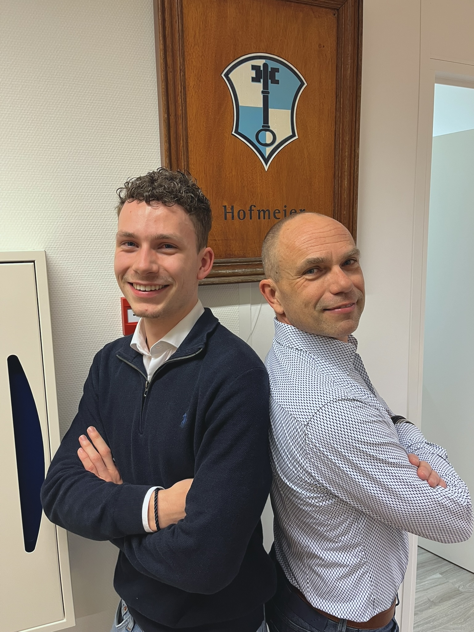 Mathijs en zijn vader Marco staan met de ruggen tegen elkaar aan voor het oude Hofmeier logo